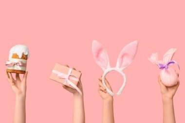 Paskalya pastası tutan kadın elleri hediye kutusu, tavşan kulakları ve pembe arka planda hediye.