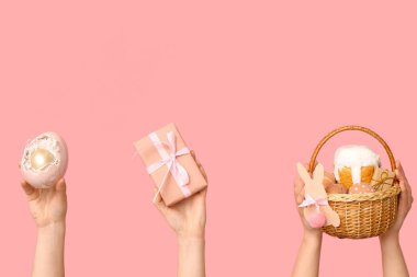 Paskalya pastası, hediye kutusu ve pembe arka planda yumurtayla sepeti tutan kadın eller.
