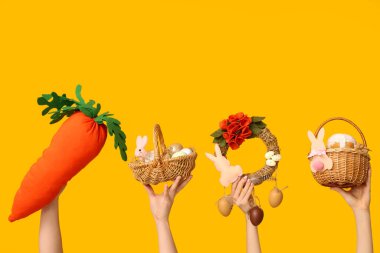 Paskalya bayramı çelenkli kadın eller, sarı arka planda oyuncak havuç ve sepetler.