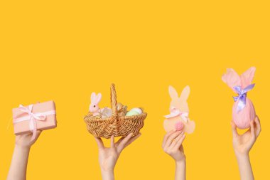 Paskalya sepetinde tavşanlı kadın elleri ve sarı arka planda hediyeler