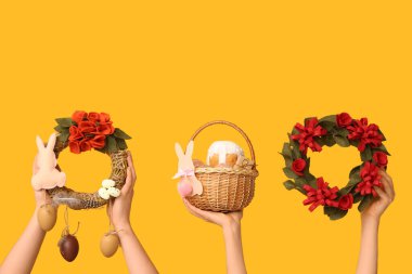 Paskalya bayramı çelenkleri ve sarı arka planda sepeti olan kadın eller.