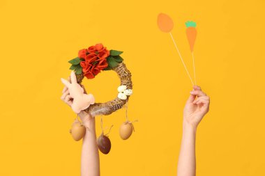 Sarı arka planda Paskalya bayramı çelengi ve dekoru olan kadın elleri