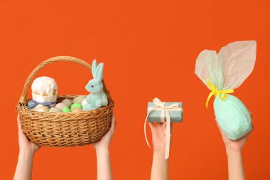 Paskalya yumurtaları ve turuncu arka planda hediyeler taşıyan kadın eli sepeti.
