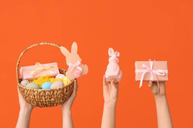 Paskalya yumurtası, tavşan ve turuncu arka planda hediye kutusu olan kadın el sepeti.