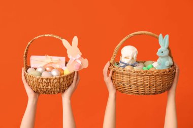 Turuncu arka planda Paskalya için sepetleri tutan kadın eller.