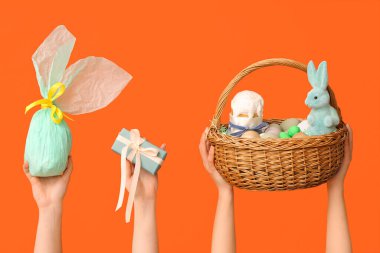 Paskalya yumurtaları ve turuncu arka planda hediyeler taşıyan kadın eli sepeti.