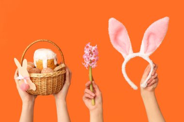 Paskalya pastası, çiçek ve turuncu arka planda tavşan kulağı olan kadın elleri.