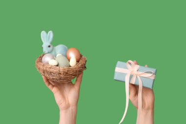 Paskalya yumurtası, tavşan ve yeşil arka planda hediye kutusu olan dişi eller yuvayı tutuyor.