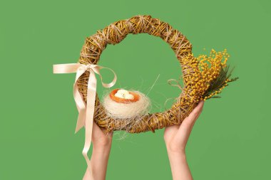 Yeşil arka planda Paskalya bayramı çelengi olan kadın elleri