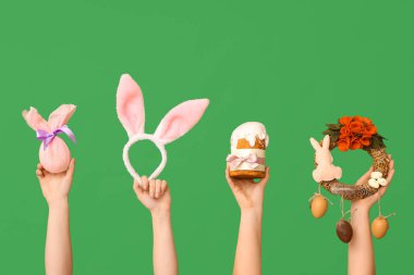 Paskalya pastası tutan kadın elleri, neşeli çelenkler, tavşan kulakları ve yeşil arka planda hediyeler.
