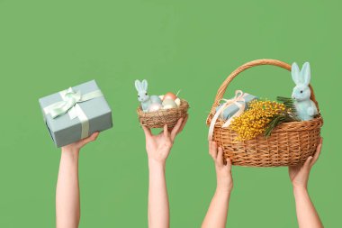 Paskalya sepetinde yeşil arka planda yuva ve hediye kutusu tutan kadın eller.