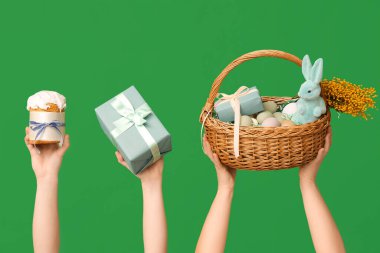 Paskalya pastası tutan kadın elleri sepet ve hediye kutusuyla yeşil arka planda