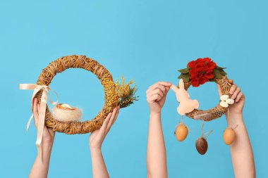 Mavi arka planda Paskalya bayramı çelenkleri olan kadın elleri