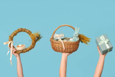 Paskalya çelengini elinde tutan kadın el sepeti ve mavi arka planda hediye kutusu.
