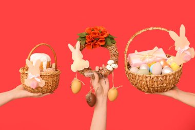 Paskalya bayramı çelengi ve kırmızı arka planda sepetleri olan kadın elleri.