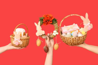 Paskalya bayramı çelengi ve kırmızı arka planda sepetleri olan kadın elleri.