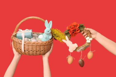 Paskalya bayramı çelengi ve kırmızı arka planda sepeti olan kadın eller.
