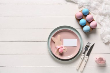 Kağıt tavşanlı Paskalya kutlaması ve beyaz ahşap arka planda boyanmış yumurtalar. Üst görünüm