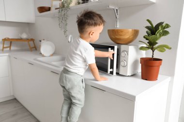 Küçük çocuk mutfakta mikrodalga fırın açıyor. Tehlikedeki çocuk