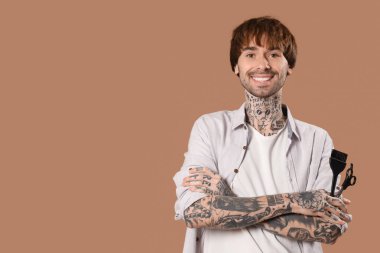 Genç dövmeli makaslı berber ve kahverengi arka planda fırça