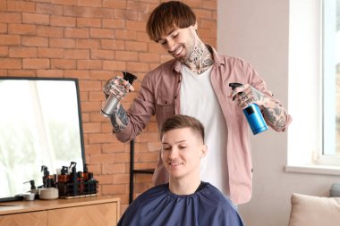 Erkek kuaför berber dükkanında müşterinin saçını spreyliyor.