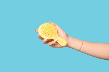 Mavi arka planda sarı saç fırçası olan bir kadın el.