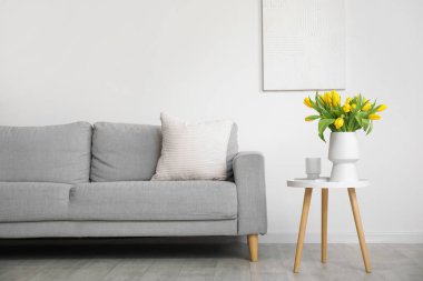 Oturma odasındaki gri kanepenin yanındaki sehpada duran sarı lalelerin güzel vazosu.