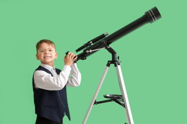 Yeşil arka planda teleskopu olan gözlüklü şirin bir okul çocuğu.