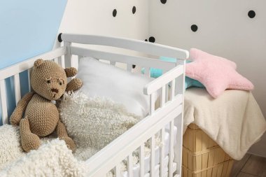 Bebek beşiğinde şirin bir oyuncak ayı çocuk odasının renkli duvarının yanında.