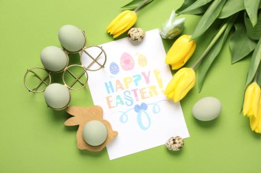 Mutlu Paskalyalar yazılı tebrik kartı, yeşil arka planda boyanmış yumurta ve laleler. Üst görünüm