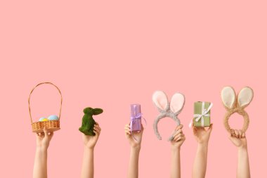 Hediyeli kadın elleri, tavşan, pembe arka planda boyalı yumurta ve kulaklıklı sepet.