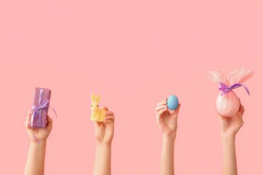 Paskalya tavşanlı kadın elleri, pembe arka planda boyanmış yumurta ve hediye yumurtası.