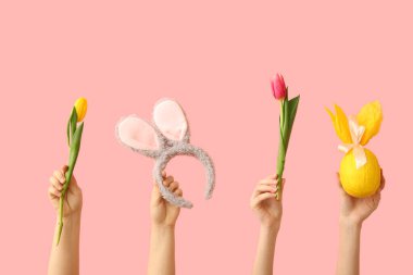 Paskalya tavşanı kulaklı kadın elleri, hediye yumurtası ve pembe arka planda laleler.