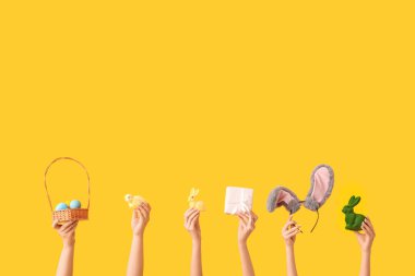 Tavşanlı kadın elleri, hasır sepete boyanmış yumurtalar, hediye, piliçler ve sarı arka planda tavşan kulaklığı.