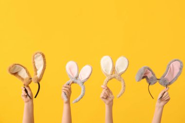 Sarı arka planda farklı tavşan kulaklıklı kadın elleri. Paskalya konsepti.