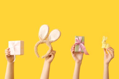 Paskalya tavşanlı kadın elleri, hediyeler ve sarı arka planda tavşan kulaklığı.