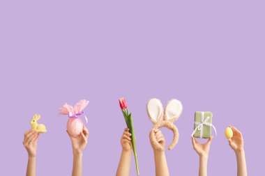 Tavşan kulaklı kadın elleri, tavşan kulaklığı, hediye, Paskalya yumurtası ve mor arka planda lale.