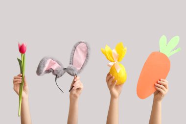 Tavşan kulaklı kadın elleri, kağıt havuç, hediye yumurtası ve gri arka planda lale. Paskalya konsepti.