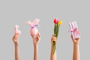 Paskalya hediyesi yumurtası, tavşan ve gri arka planda bir buket lale olan kadın elleri.