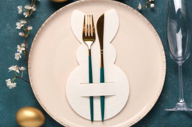 Mavi grunge arka planında Paskalya yumurtaları ve çiçek açan kiraz dalı olan masa ayarı, yakın plan.