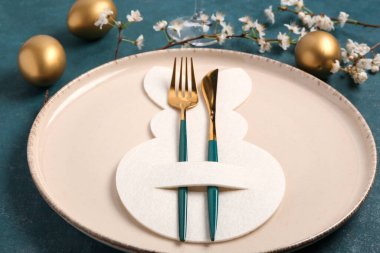 Mavi grunge arka planında Paskalya yumurtaları ve çiçek açan kiraz dalı olan masa ayarı, yakın plan.