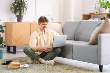 Dizüstü bilgisayarı olan erkek öğrenci evde internette ders çalışıyor.