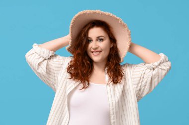 Mavi arka planda şapkalı, gülümseyen kızıl saçlı kadın.