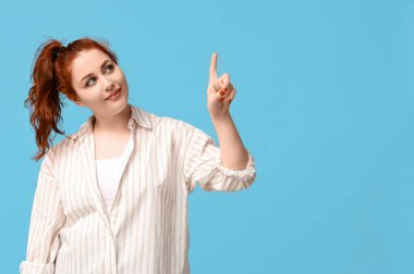 Mavi arka plandaki bir şeyi işaret eden at kuyruklu güzel kızıl saçlı kadın.