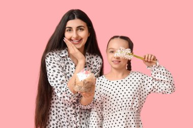 Mutlu gülümseyen genç kadın ve kızı pembe arka planda Paskalya pastası ve çiçek tutuyorlar.