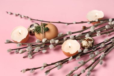 Pussy willow branches with Easter eggs and burning candles on pink background