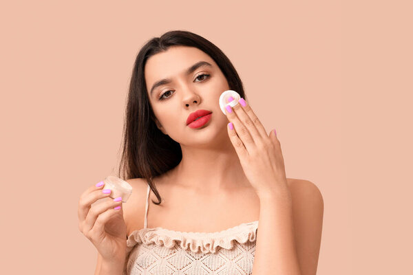 Beautiful young woman with sponge and powder on beige background
