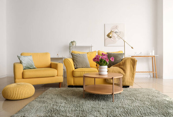 Interior of light living room with sofa, armchair and tulips on table