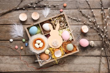 Box with Easter eggs, pussy willow branches and burning candles on wooden background