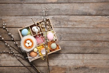 Pussy willow branches and bowl with Easter eggs on wooden background